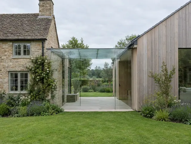 Frameless structural glass link joining a stone cottage to a timber-clad extension