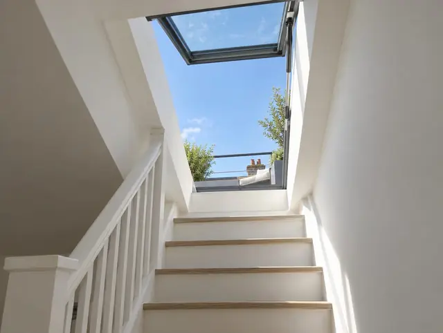 Open hinged roof access rooflight at the top of a white staircase