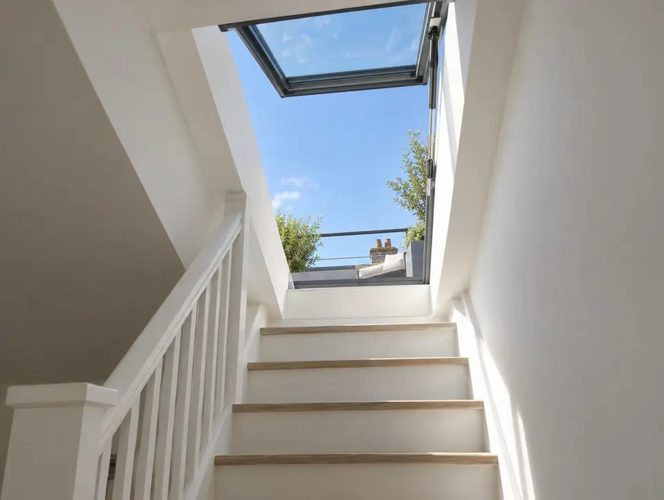 Open hinged roof access rooflight at the top of a white staircase